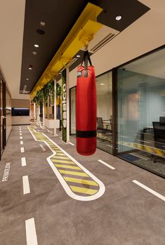 a red boxing bag hanging from the ceiling in an office building hallway with yellow and black accents