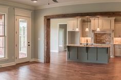 an empty kitchen and living room in a house with hard wood flooring, large windows, and white cabinets