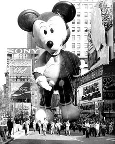 a large mickey mouse balloon being flown in the air with other people walking around it