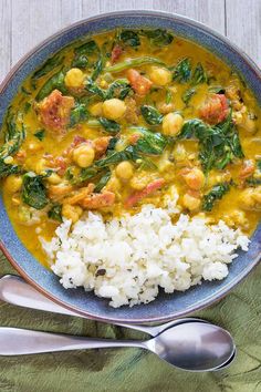 a bowl filled with white rice and spinach next to a spoon on top of a table