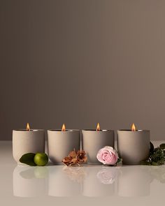 five candles are lined up next to each other with flowers and leaves on the table