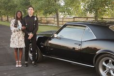 a man and woman standing next to a black car