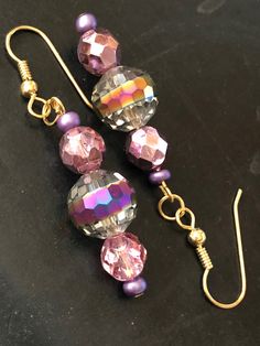 A lovely metallic drop earrings with loads of sparkle to dress up any holiday outfit. A fire polished central bead exhibits a purple tone which blends nicely with the faceted purple metallic beads on each side. The ear wire is nickel-free gold plate. Party Jewelry With Iridescent Ear Wire, Iridescent Party Earrings, Party Beaded Drop Earrings With Ear Wire, Beaded Drop Earrings For Party, Party Crystal Dangle Earrings With Ear Wire, Party Beaded Drop Earrings With Faceted Beads, Handmade Iridescent Crystal Earrings For Party, Gold Beaded Earrings With Faceted Beads For Party, Gold Party Beaded Earrings With Faceted Beads