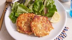 two crab cakes on a white plate next to a green leafy salad and fork