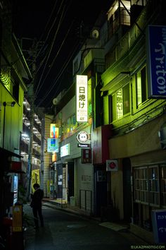 a person walking down an alley way at night with neon signs on the buildings in the background