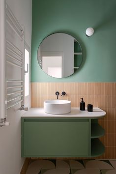 a bathroom with a round mirror above the sink and green walls, along with two black soap dispensers