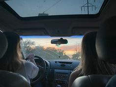 two women sitting in the driver's seat of a car, looking out the window