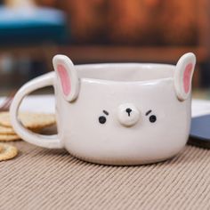 a white mug with ears on it sitting next to crackers