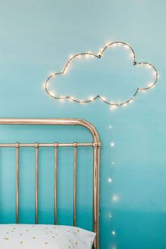 a bed with a gold headboard and a cloud shaped string light above it on the wall