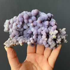 a hand is holding up a cluster of purple beads that look like they are floating in the air