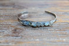 "Gemstone open gold or silver bangle with pieces of light gray Labradorite with flashes of blue and green. The setting is on a long rectangle that is 2\" long and a little under 1/4\" narrow, it is petite and slim. The cuff is gold or silver plated stainless steel and adjustable, 2\" x 2 1/2\" circumference.  The bracelet is made with natural stone each one has slight variations in size and shape. Your bracelet will be unique." Handmade Silver Bracelets For Healing, Handmade Labradorite Bangle Jewelry, Unique Labradorite Bangle Jewelry, Silver Moonstone Bangle, Blue Labradorite Bracelet, Spiritual Labradorite Bracelet, Silver Labradorite Bangle Bracelets, Silver Labradorite Bangle Bracelet, Labradorite Bracelet Jewelry Gift