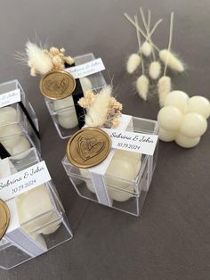 three small clear boxes with candles in them on a table next to some flowers and feathers