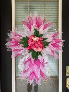 a pink and white wreath is hanging on the front door with some flowers in it