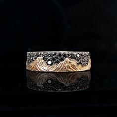 a gold and silver ring with mountains in the middle on a black reflective surface,