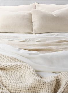 an unmade bed with white sheets and pillows