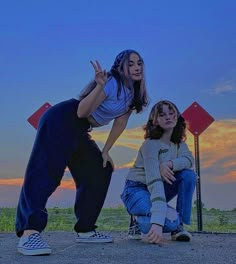 two young women sitting on the ground with their hands in the air and one standing behind them