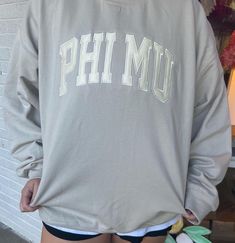 the back of a woman's shirt that says phi mu on it and has her hands in her pockets