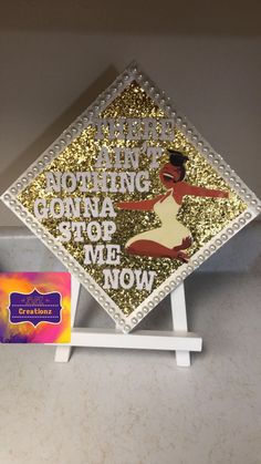 there is a gold and white graduation cap on top of a book stand with a card in front of it