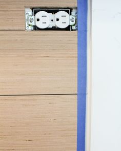 an electrical outlet on the side of a wooden wall with blue tape and two white outlets