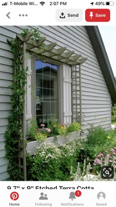 an open window on the side of a house covered in vines and flowers, next to a garden