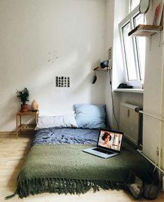 a laptop computer sitting on top of a bed in a room with white walls and wooden floors