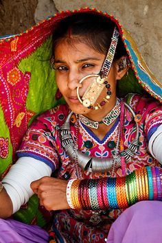 a woman in colorful clothing sitting on the ground with her nose ring and bracelets around her neck