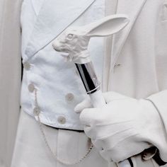 a man in a white suit holding a black and silver pipe with a rabbit head on it