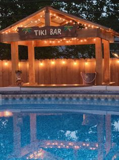 the tiki bar is lit up at night next to a swimming pool with lights on it