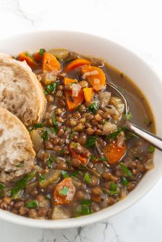 a white bowl filled with lentula and carrots next to a piece of bread