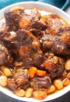 a white bowl filled with meat and beans on top of a blue cloth covered table