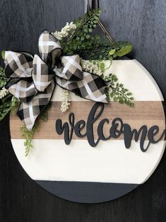 a welcome sign hanging on the side of a door with greenery and ribbon around it