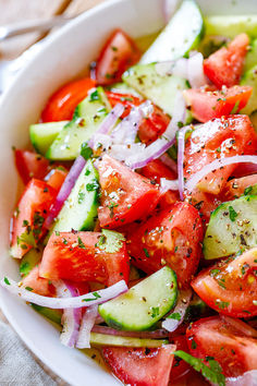 a white bowl filled with cucumber, tomato and onion salad on top of a table