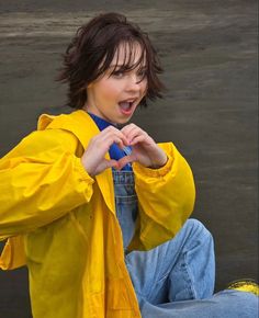 a young woman sitting on the ground wearing a yellow jacket