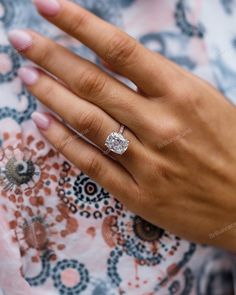 a woman's hand with a diamond ring on her left hand, wearing a floral dress