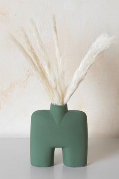 a green vase with some white feathers in it's mouth and on the table