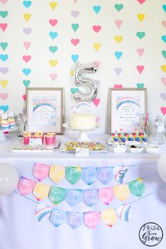 a table topped with cake and cupcakes next to a wall covered in hearts