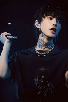 a man with tattoos on his arm holding a microphone and wearing a black t - shirt