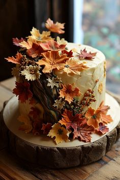 there is a cake decorated with fall leaves on the wooden table next to a window