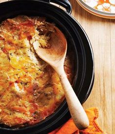 a casserole with cheese and meat in a black crock pot on a wooden table