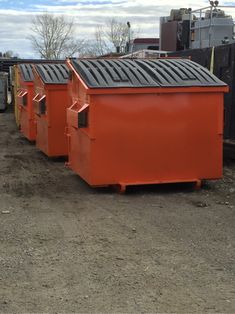 three orange dumpsters sitting on top of a dirt field