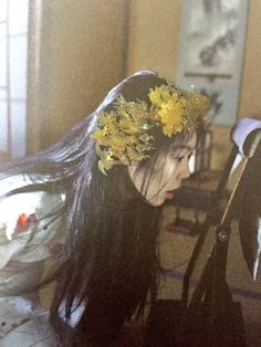 a woman with flowers in her hair is sitting on the floor next to a pair of scissors