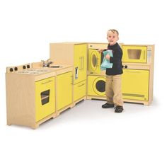 a young boy standing in front of a yellow play kitchen with an oven and washer