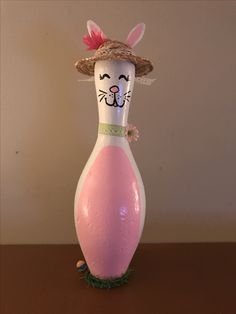 a pink vase sitting on top of a wooden table next to a white wall with a cat face painted on it