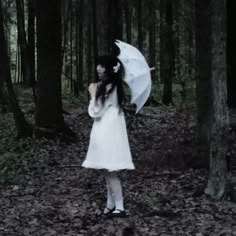 a woman in a white dress holding an umbrella and standing in the middle of a forest