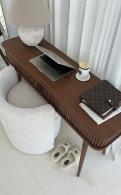 a laptop computer sitting on top of a wooden desk next to a white chair and lamp