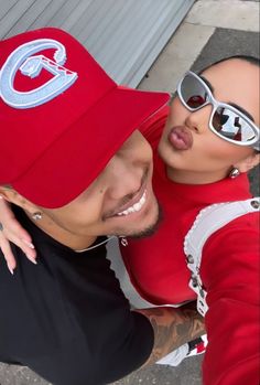 a man and woman are taking a selfie with sunglasses on their heads, one is wearing a red baseball cap