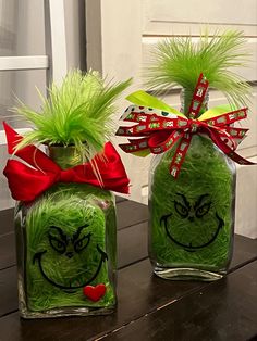 two glass vases with green grass in the shape of grin face and red bow