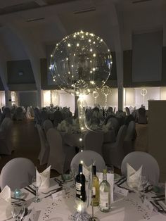 an empty banquet room is set up with white linens and round tables, lighted by lights