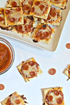 several square pieces of pizza on a plate next to a small bowl of tomato sauce