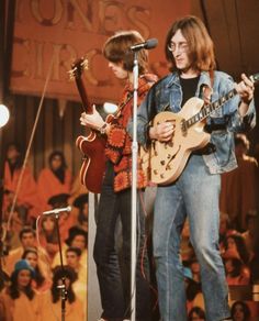 two young men are playing guitars on stage while an audience watches from the sidelines